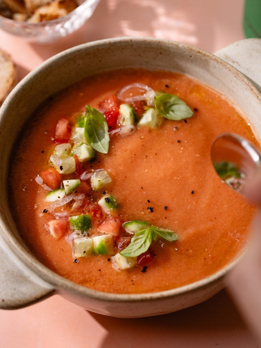 Cuillère plongeant dans un gaspacho andalou servi avec légumes croquants et basilic
