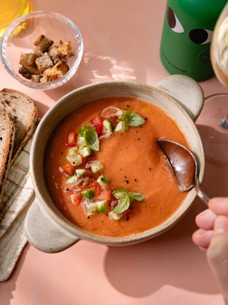 Cuillère plongeant dans un gaspacho andalou servi avec légumes croquants et basilic