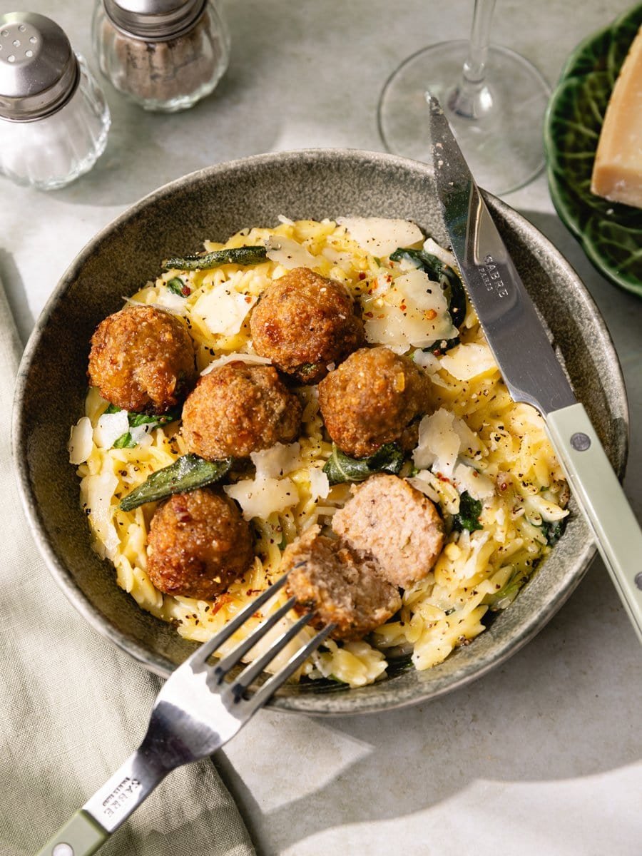 Boulette de poulet coupée en deux pour révéler une chair moelleuse servie avec un orzotto crémeux au parmesan.