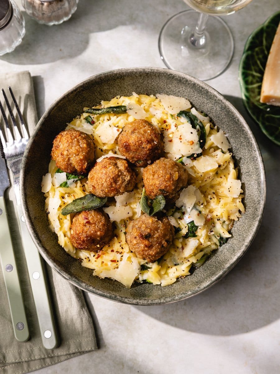 Assiette d'orzotto crémeux au parmesan garnie de boulettes de poulet maison, d'épinards, de sauge croustillante et de parmesan.