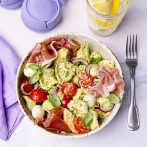 Assiette de salade de tortellini aux tomates cerise, billes de mozzarella, jambon italien, pesto vert, oignon rouge et cœurs d'artichauts