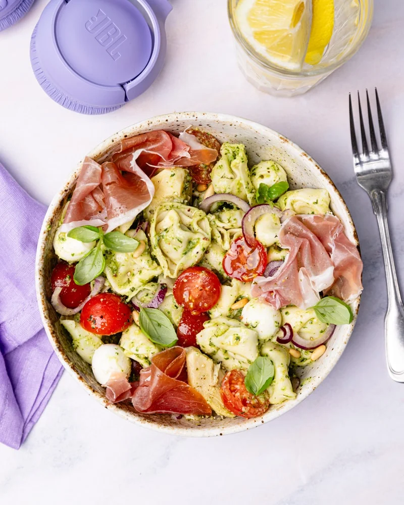 Assiette de salade de tortellini aux tomates cerise, billes de mozzarella, jambon italien, pesto vert, oignon rouge et cœurs d'artichauts