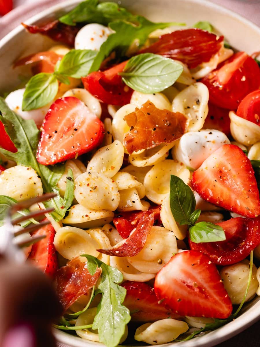 Gros plan d'une salade de pâtes caprese aux fraises avec mozzarella, tomates cerises, roquette, basilic frais et jambon cru croustillant