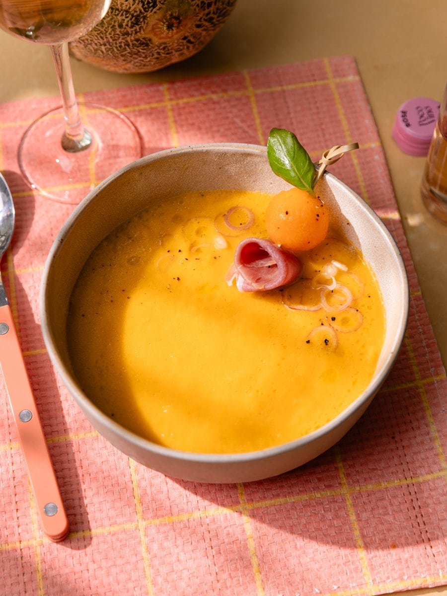 Bol de gaspacho au melon accompagné d'une bille de melon, de jambon cru et de basilic