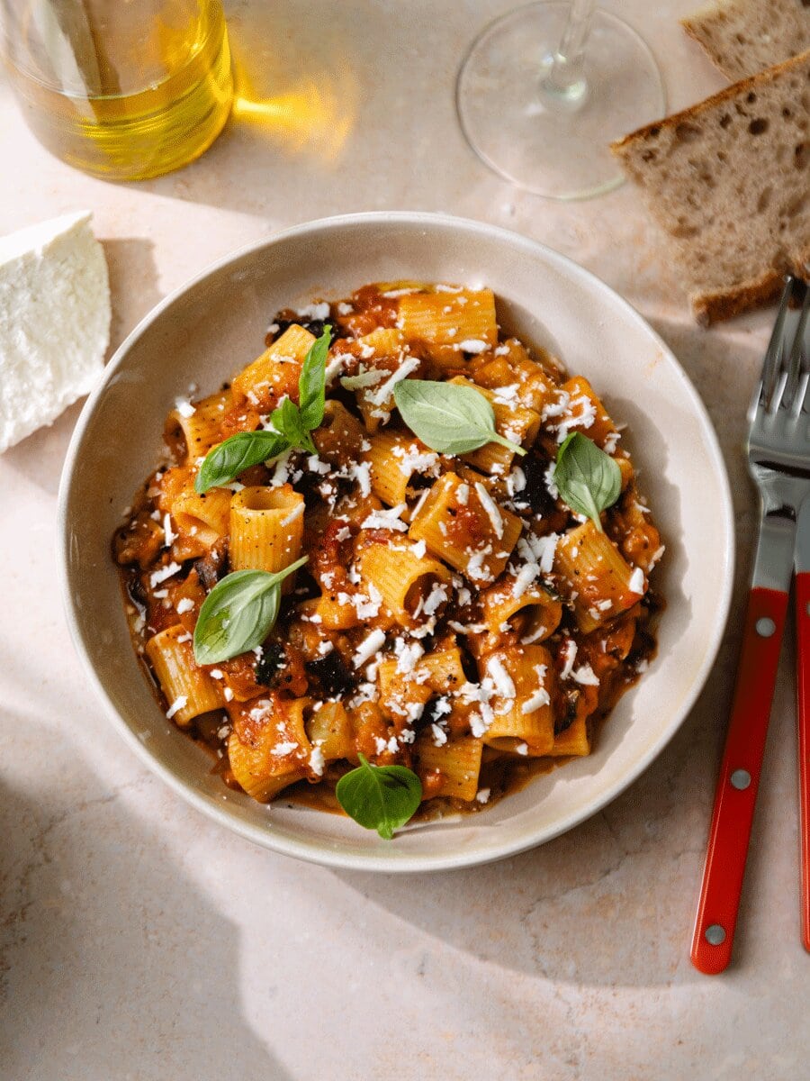 Pâtes alla Norma aux aubergines, sauce tomate maison et ricotta salata râpée, servies avec basilic frais dans une assiette, spécialité sicilienne gourmande