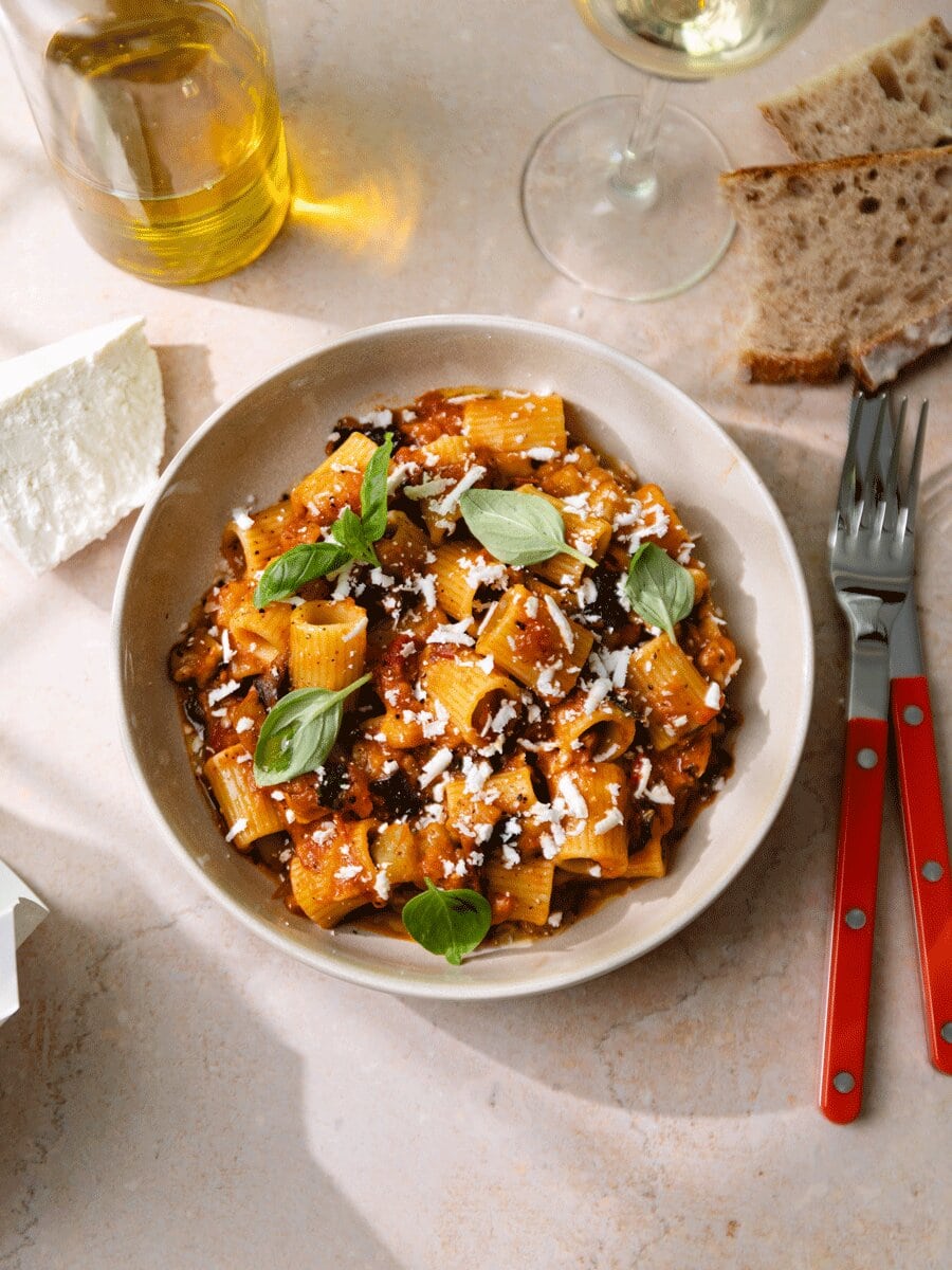 Pâtes alla Norma aux aubergines, sauce tomate maison et ricotta salata râpée, servies avec basilic frais dans une assiette, spécialité sicilienne gourmande