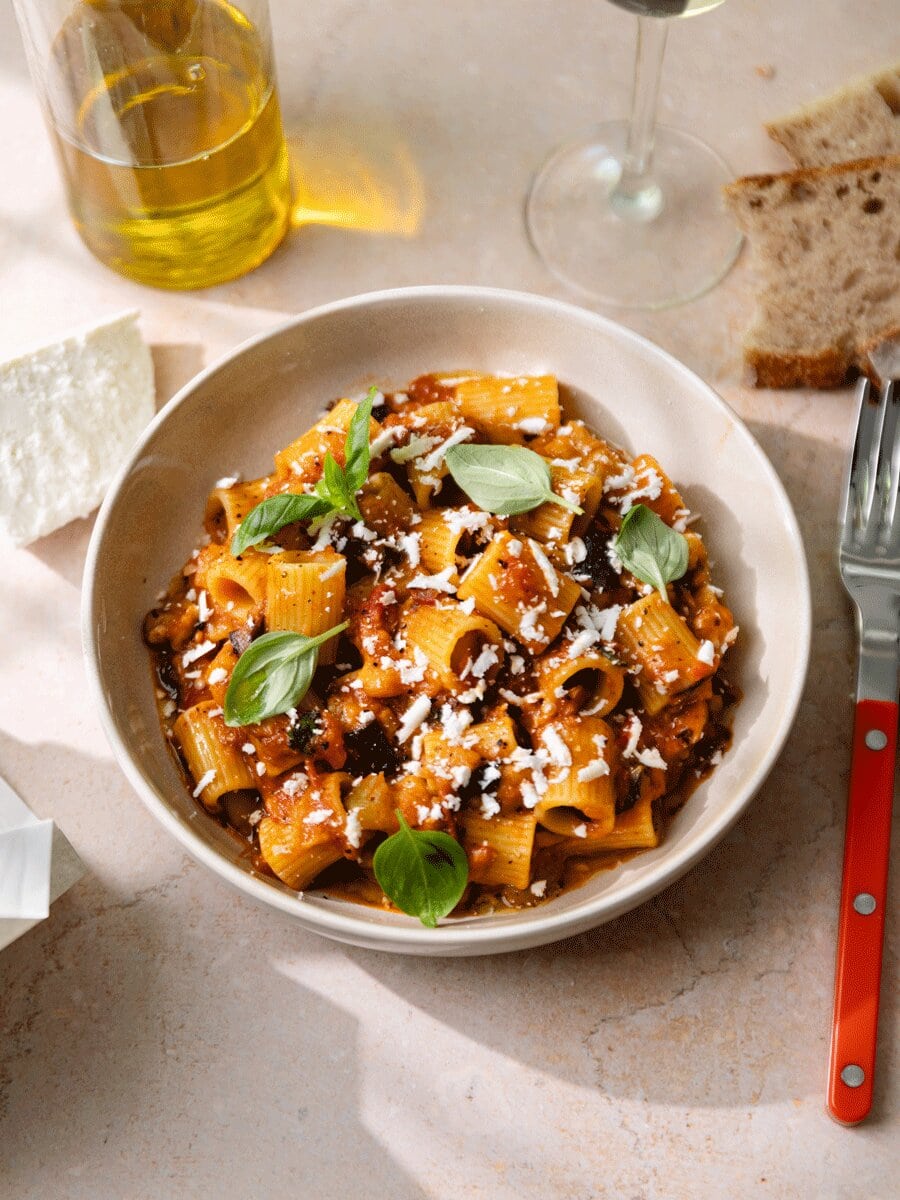 Pâtes alla Norma aux aubergines, sauce tomate maison et ricotta salata râpée, servies avec basilic frais dans une assiette, spécialité sicilienne gourmande