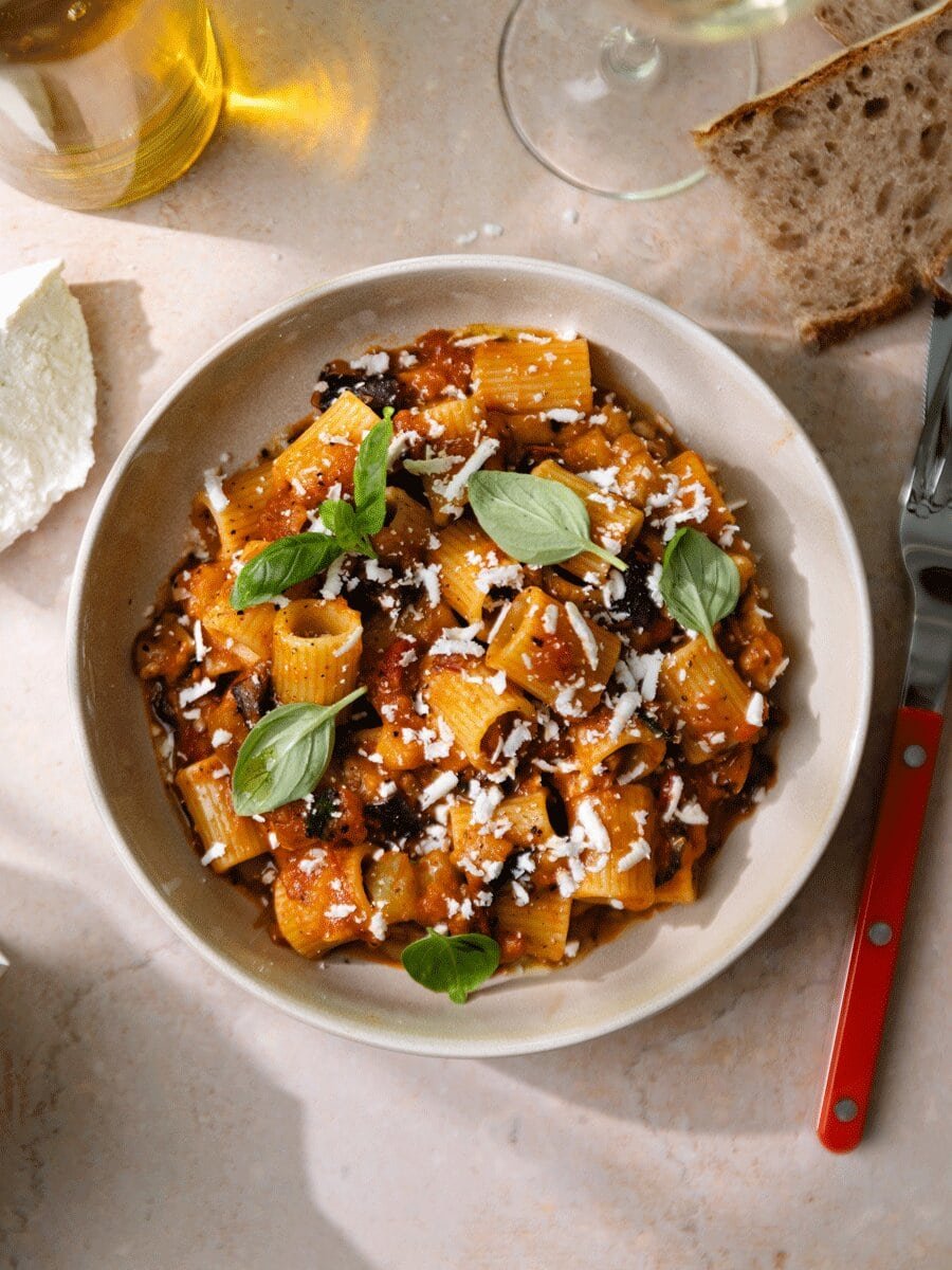 Pâtes alla Norma aux aubergines, sauce tomate maison et ricotta salata râpée, servies avec basilic frais dans une assiette, spécialité sicilienne gourmande