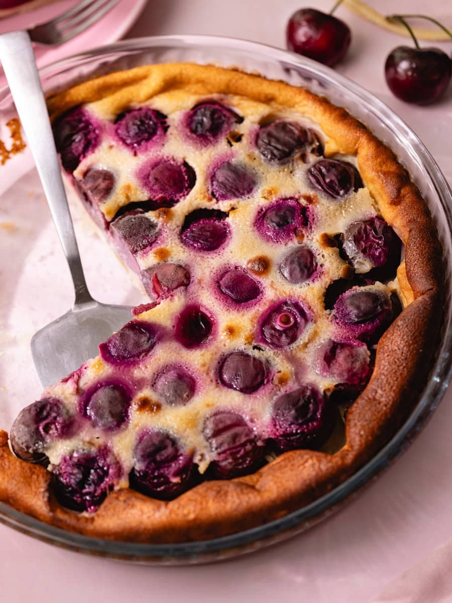 Clafoutis aux cerises moelleux dans un plat à tarte, avec cerises entières légèrement caramélisées et pâte dorée maison