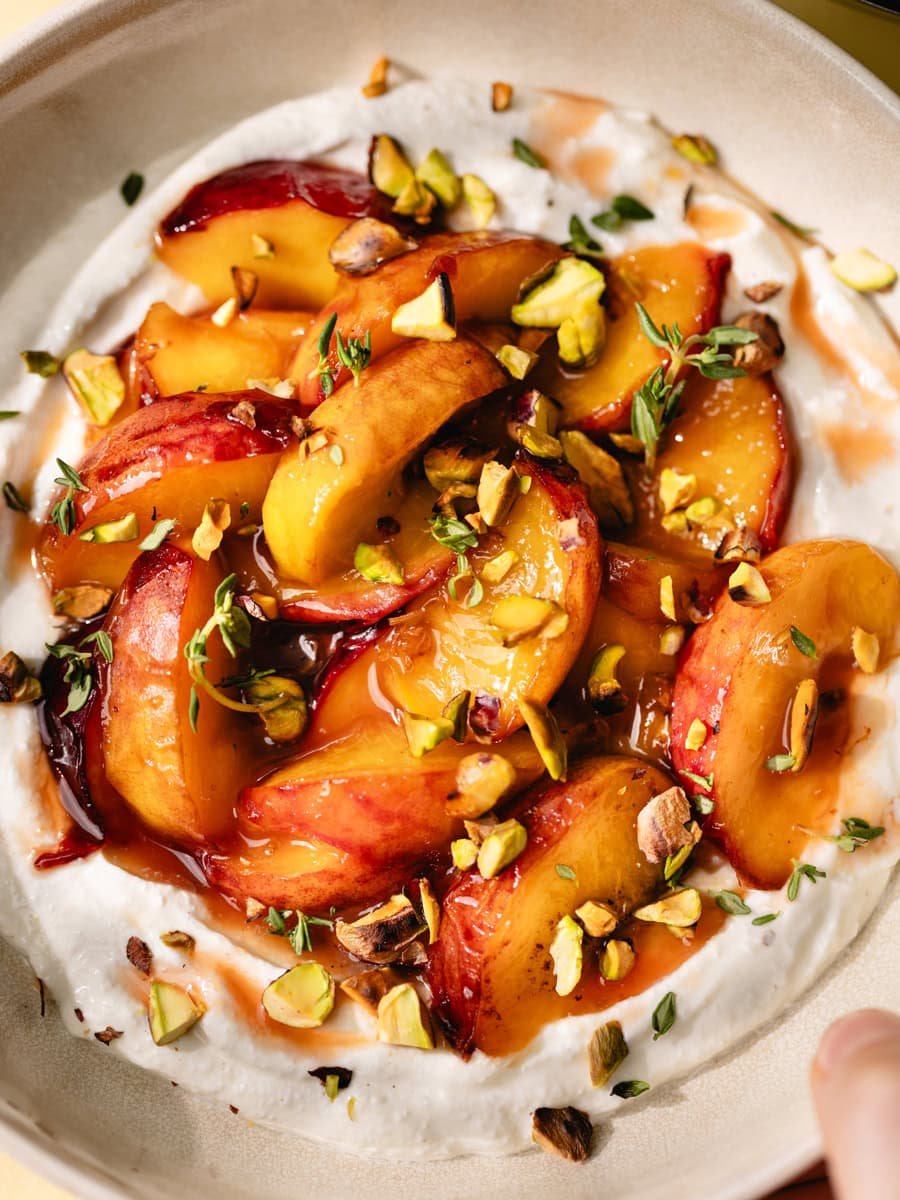 Pêches fraîches, pistaches et crème dans un dessert gourmand et coloré. Parfait pour une touche frui.