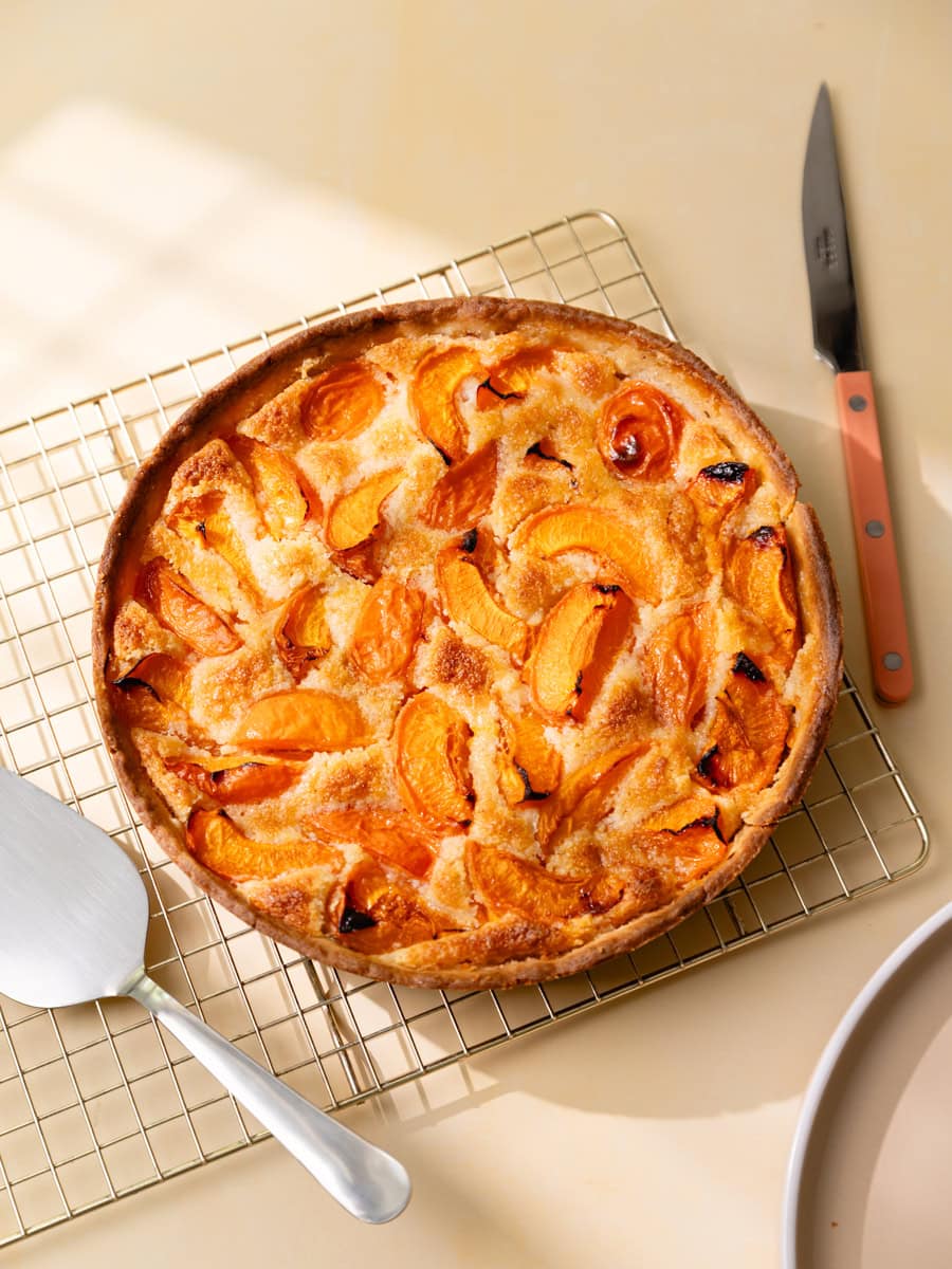 Tarte aux abricots maison et crème d’amande dorée vue du dessus, servie dans un plat blanc avec des quartiers d’abricots rôtis et légèrement caramélisés