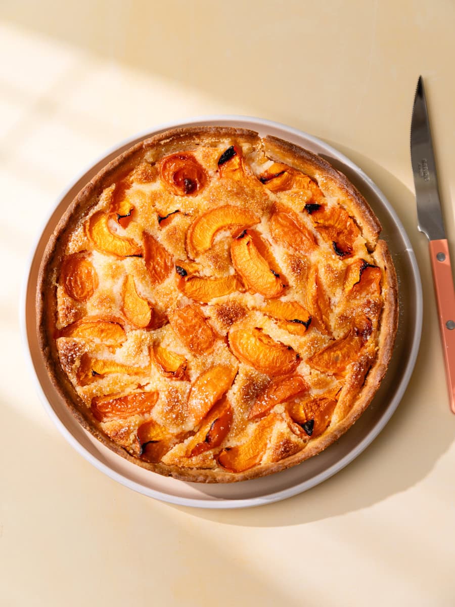 Tarte aux abricots maison et crème d’amande dorée vue du dessus, servie dans un plat blanc avec des quartiers d’abricots rôtis et légèrement caramélisés