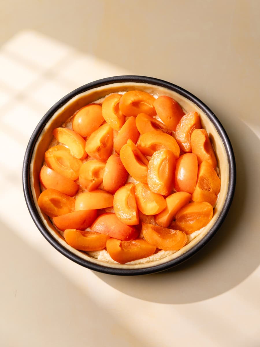 Tarte aux abricots avant cuisson garnie de crème d’amande et de quartiers d’abricots frais disposés dans un moule à tarte, vue du dessus