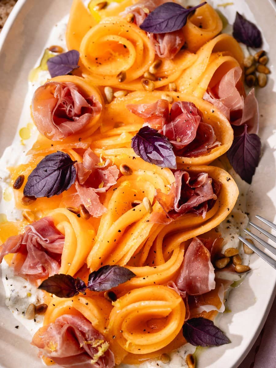 Carpaccio de melon servi sur un lit de stracciatella avec jambon cru, pignons de pin grillés, basilic frais et zeste de citron.