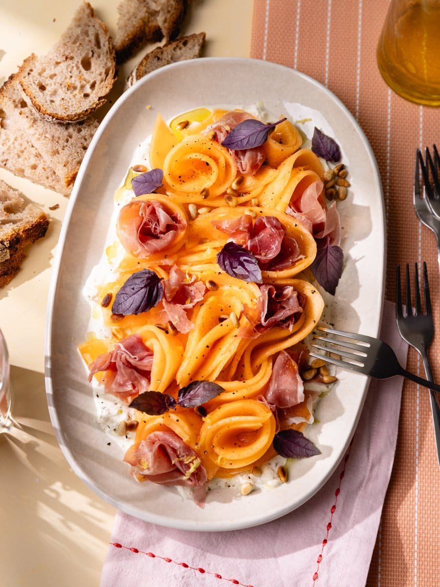 Carpaccio de melon servi sur un lit de stracciatella avec jambon cru, pignons de pin grillés, basilic frais et zeste de citron.