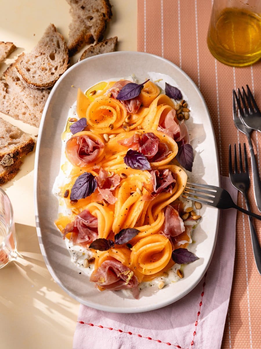 Carpaccio de melon servi sur un lit de stracciatella avec jambon cru, pignons de pin grillés, basilic frais et zeste de citron.