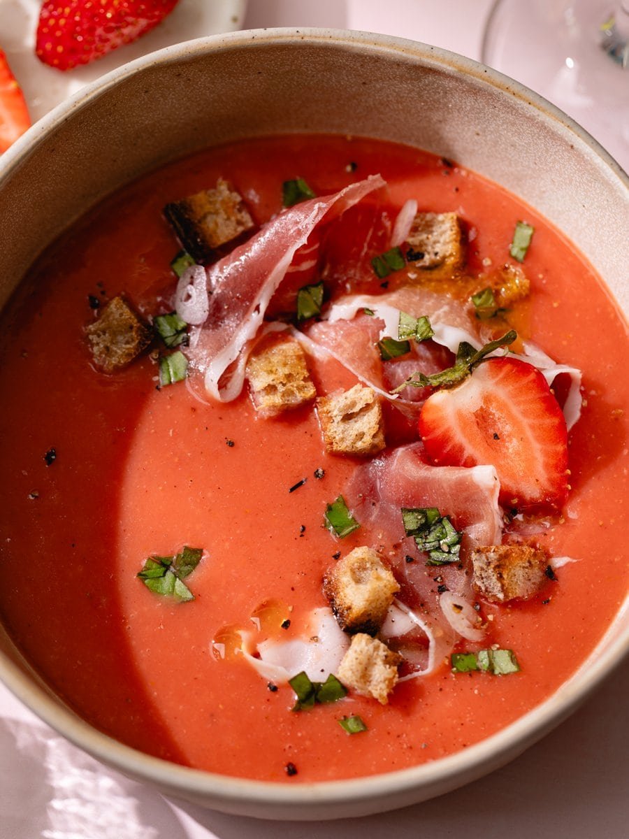 Bol de gaspacho aux fraises et tomates garni de jambon cru, croûtons grillés, basilic frais et huile d'olive