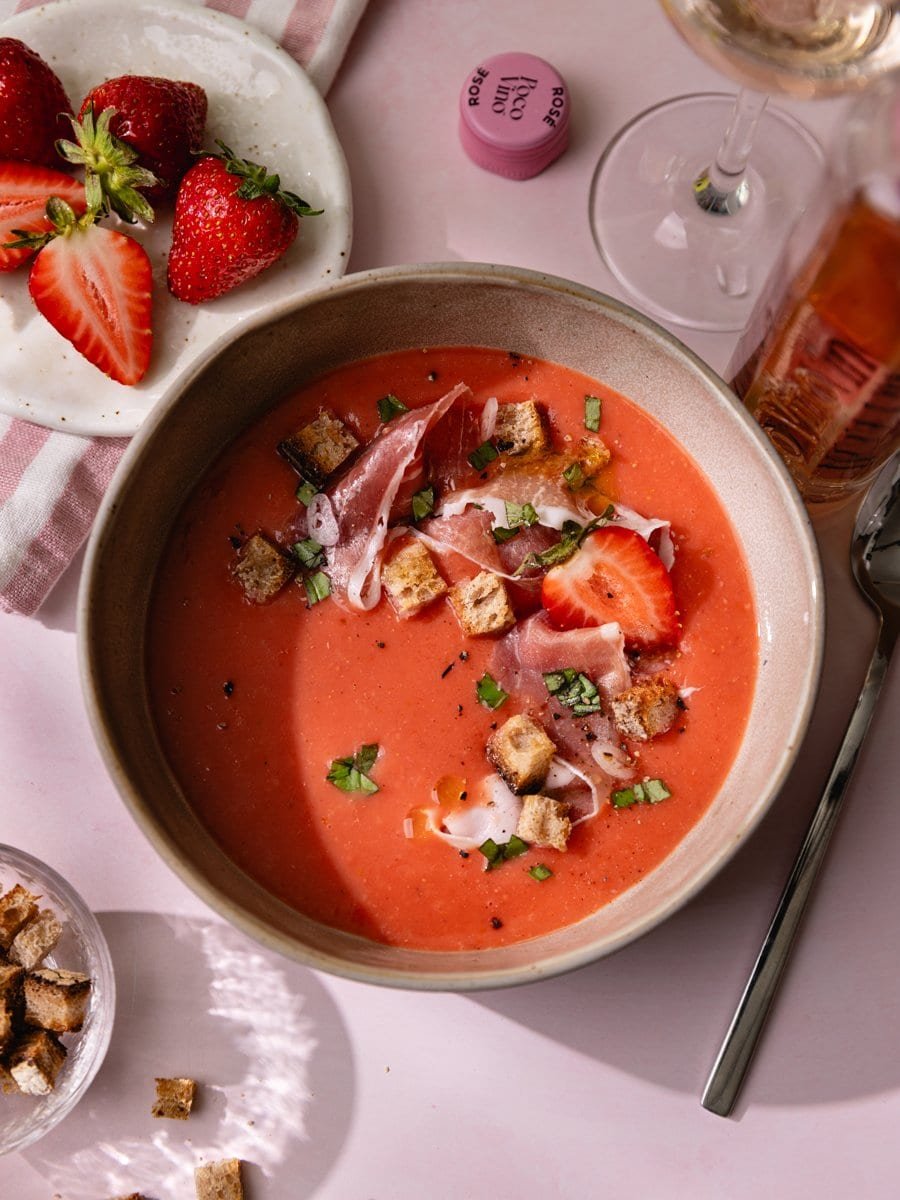 Vue plongeante sur un gaspacho rose aux tomates et fraises avec jambon cru, basilic ciselé et croûtons