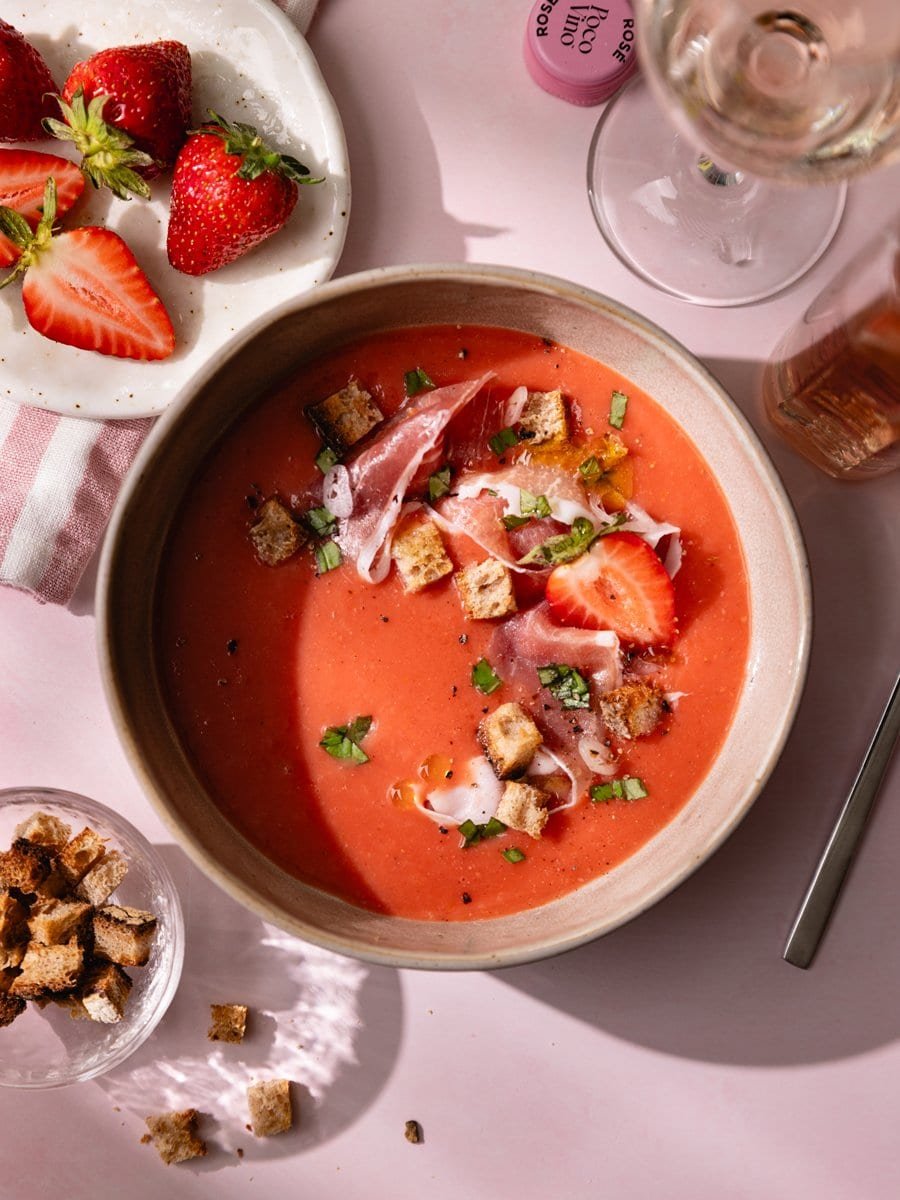 Table estivale avec gaspacho aux fraises et tomates, verre de rosé, fraises fraîches et croûtons maison