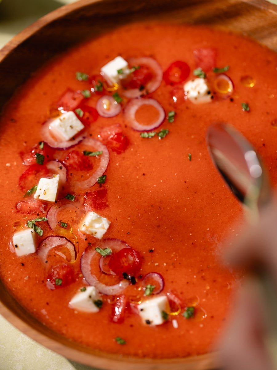Gros plan sur un gaspacho pastèque tomate garni de feta, oignon rouge et huile d'olive