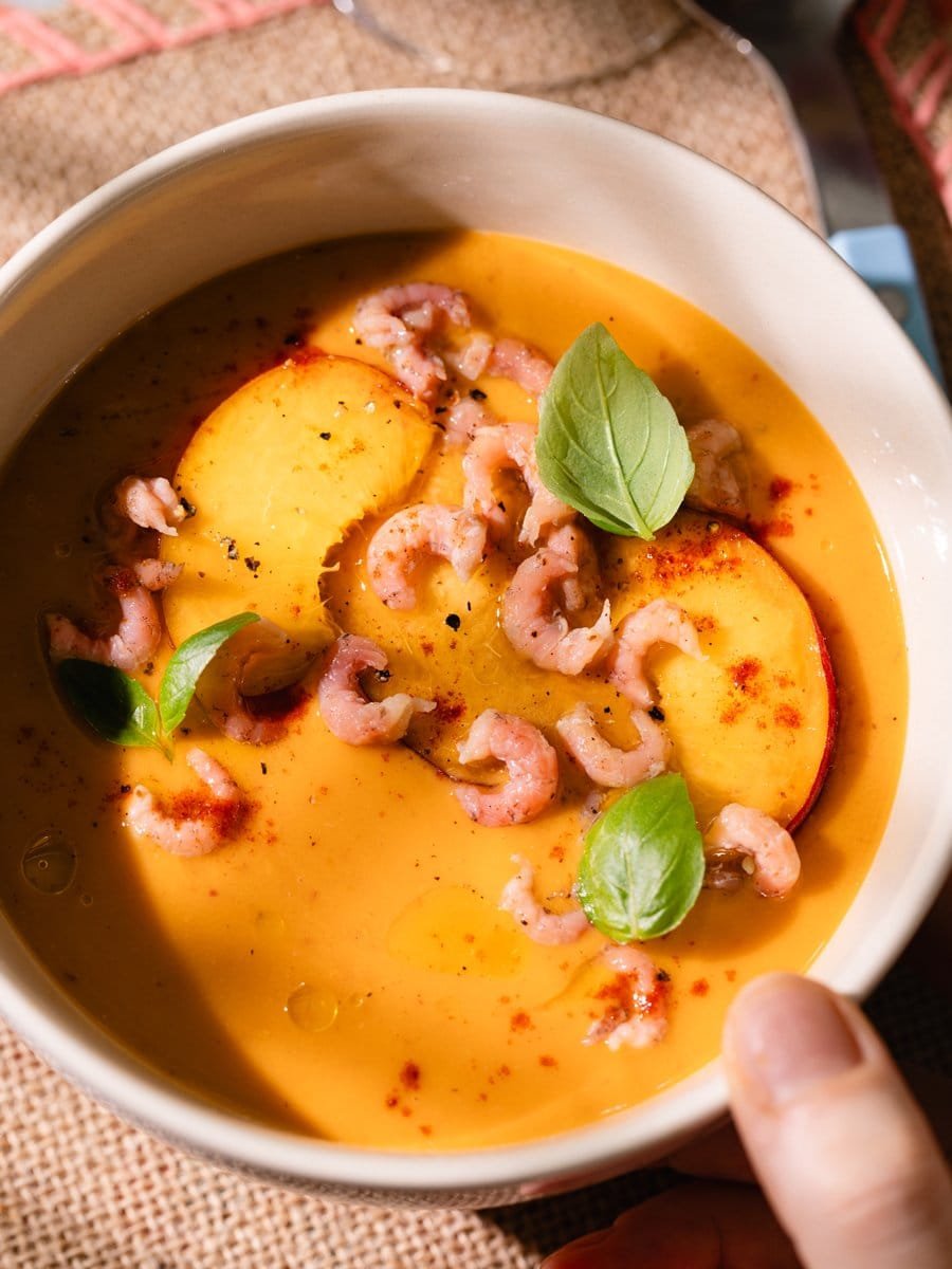 Bol de gaspacho de pêches garni de crevettes grises, tranches de pêche, basilic frais et paprika