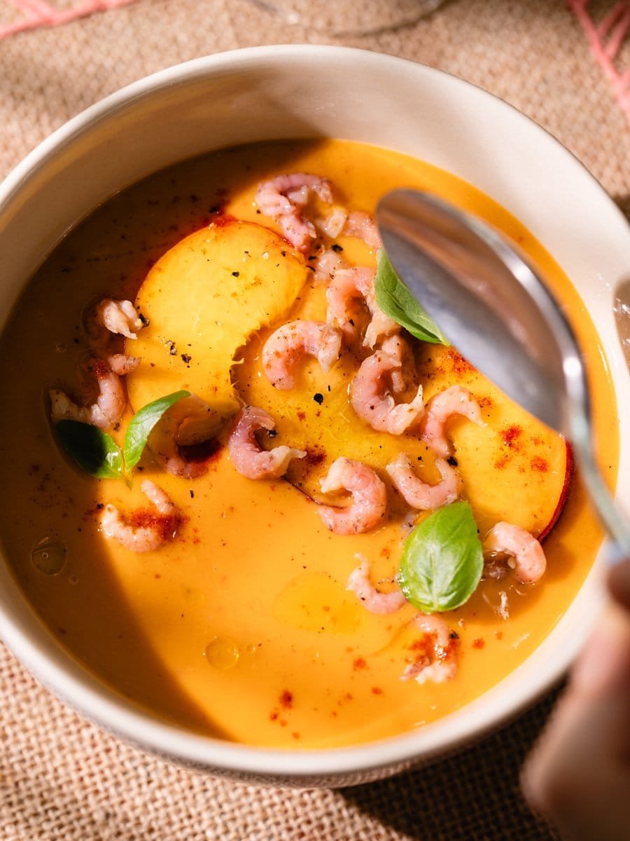 Cuillère plongeant dans un gaspacho de pêches aux crevettes grises et paprika