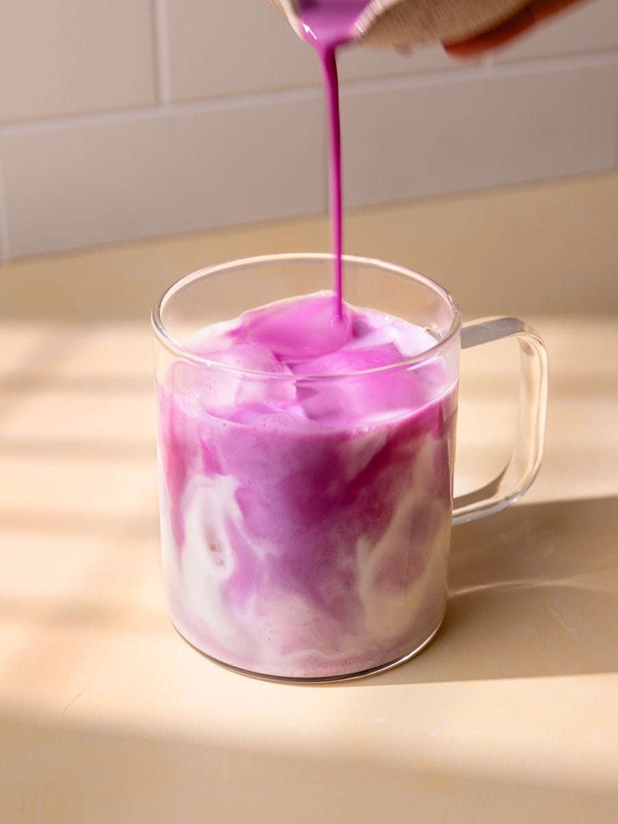 Iced ube latte maison avec lait et purée d’ube violette versée sur des glaçons dans une tasse en verre