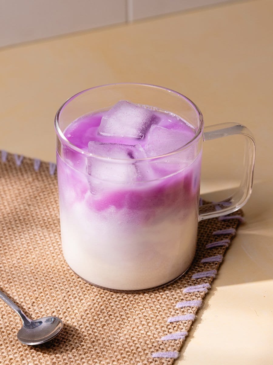 Verre d’iced ube latte violet avec glaçons et effet marbré à l’ube sur fond clair