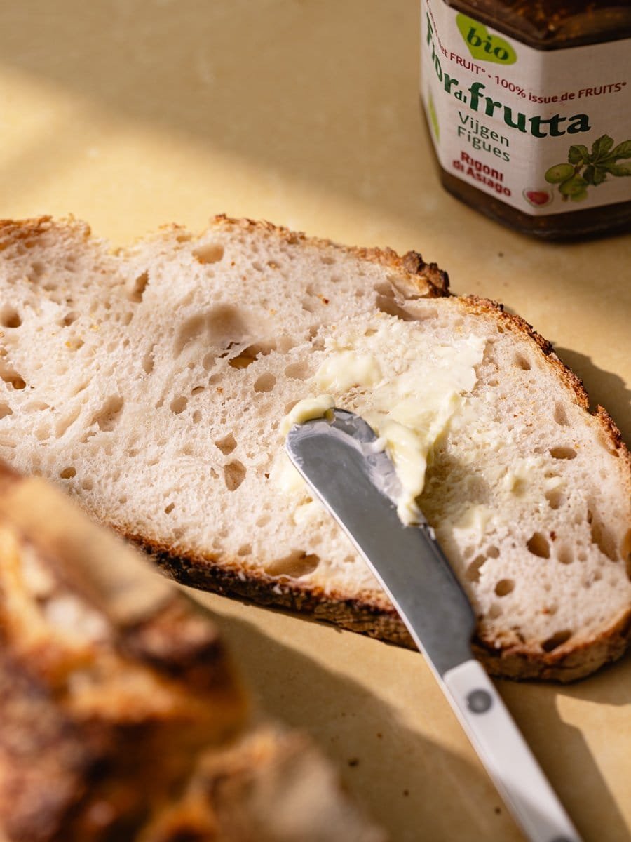 Tranche de pain blanc au levain tartinée de beurre avec couteau à beurre sur une table en pierre claire