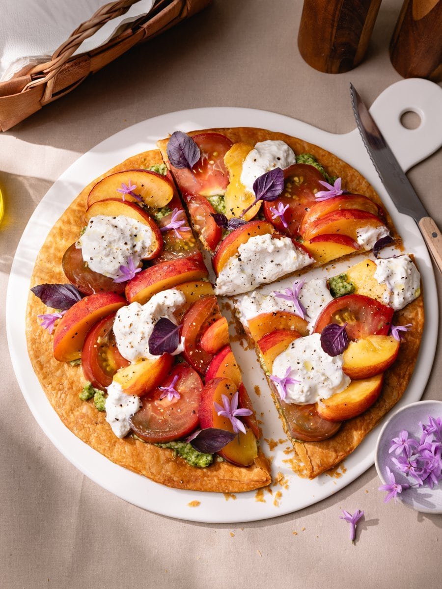 Tarte fine tomates et pêches découpée en parts avec stracciatella et pesto