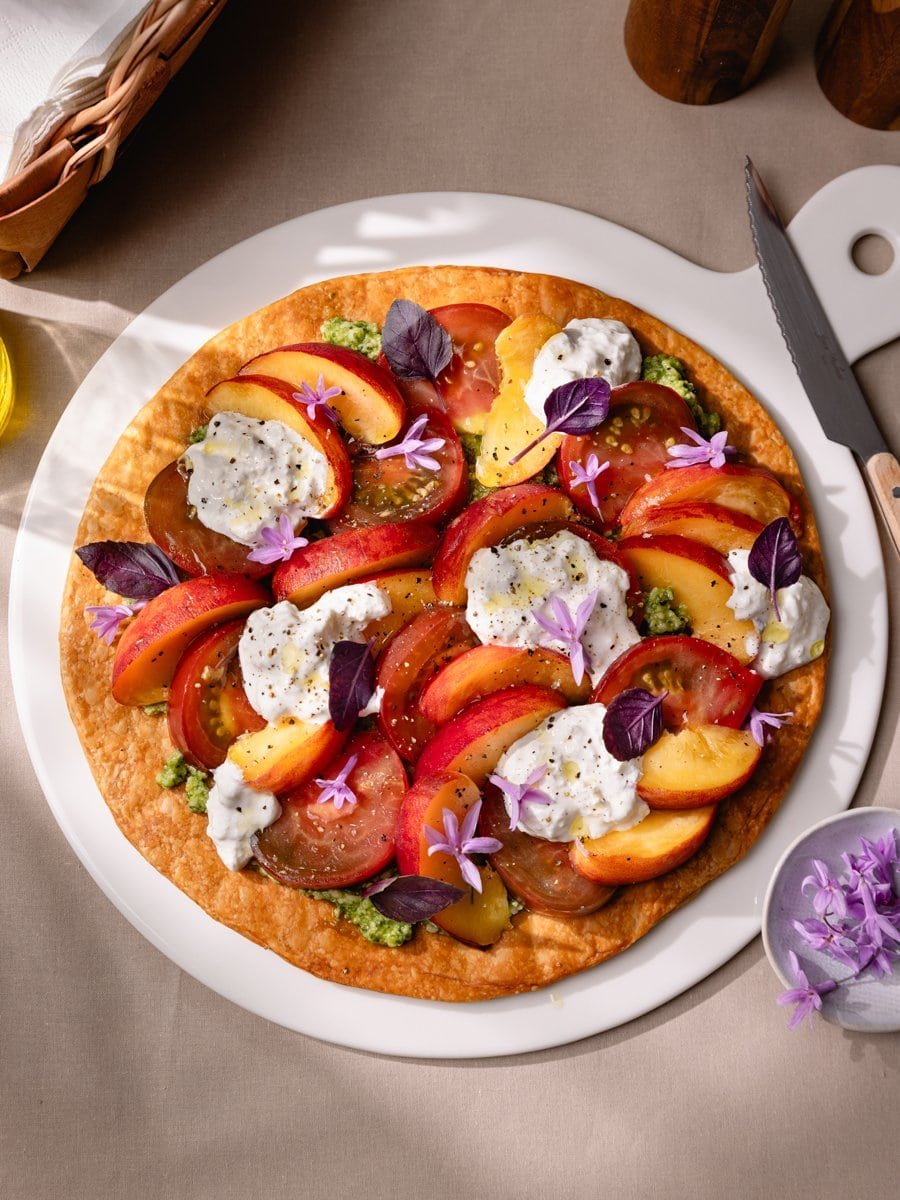Tarte fine aux pêches, tomates anciennes et stracciatella servie sur une grande assiette